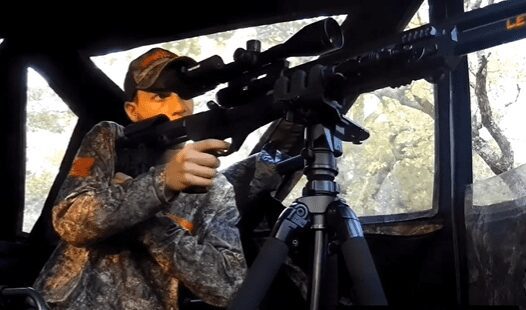 Man looks through scope of a gun that is sitting on a tripod