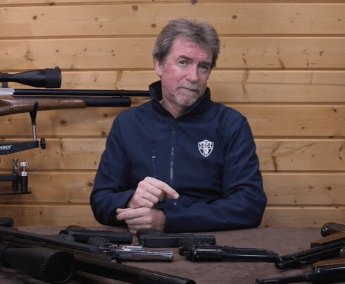Man sits at a table with a variety of airguns